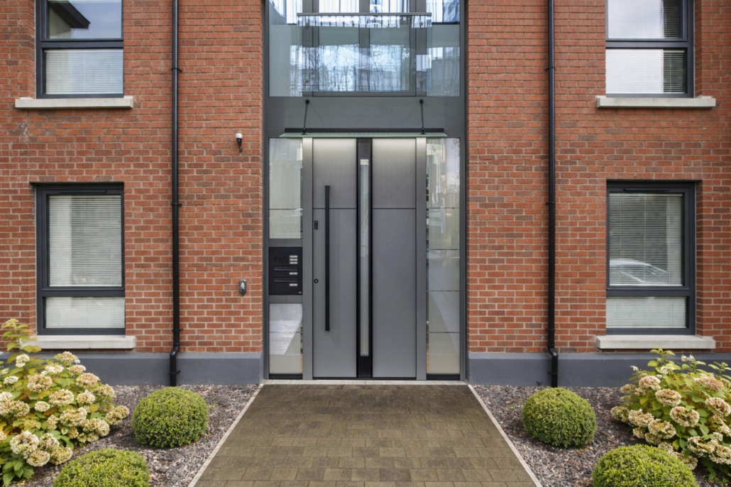 Porte d’entrée grise avec boîte aux lettres sur un immeuble à façade en briques rouges